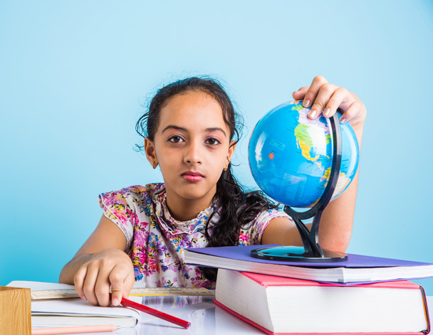 Indiase meisje student kijken naar educatieve Globe en zittend aan tafel met boeken, tafellamp en melk mok, Aziatische meisje kind studeren geografie, nieuwsgierig Aziatisch meisje studeren geografie met Globe - Foto, afbeelding