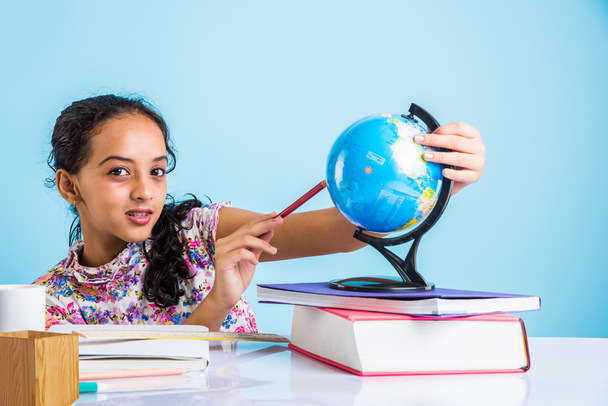Indian Girl student patrząc na świecie edukacji i siedząc przy stole z książek, Lampa stołowa i kubek mleka, Asian Girl dziecko studiowanie geografii, ciekawy Asian Girl studiowanie geografii z globu - Zdjęcie, obraz