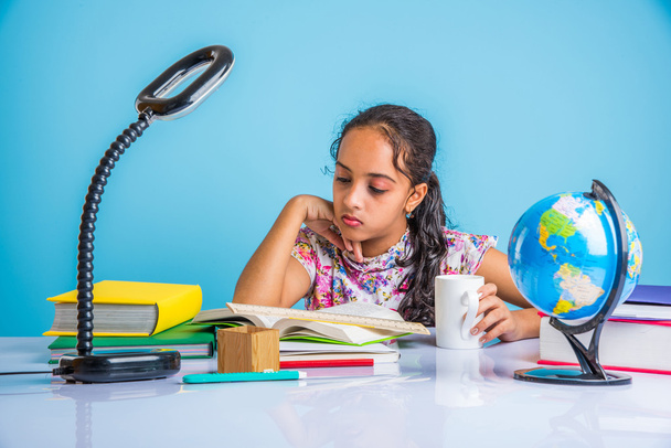 education and home concept - stressed student girl with books, indian girl child tired of studying or doing homework, asian girl studying and stressed, with globe toy and coffee mug - Photo, Image