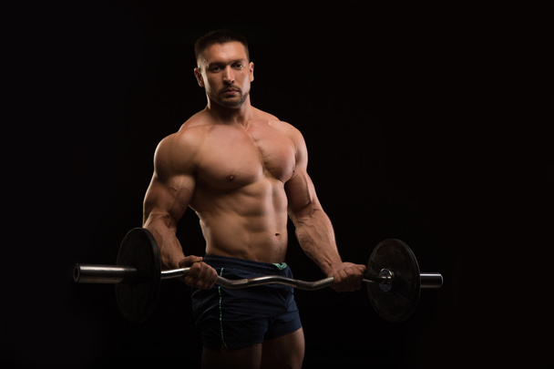 schöner muskulöser Bodybuilder posiert auf schwarzem Hintergrund - Foto, Bild