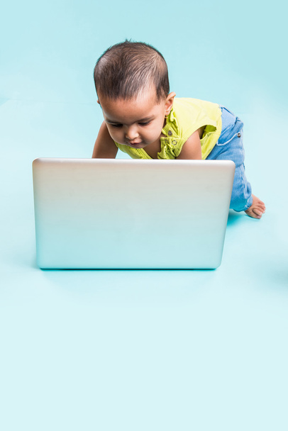 bebê sentado no chão com um laptop, menina indiana com laptop sobre fundo azul, menina indiana brincando com laptop, menina asiática com laptop
 - Foto, Imagem