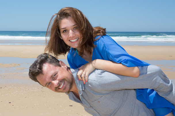 feliz casal sorrindo para o homem da praia dando piggyback
 - Foto, Imagem