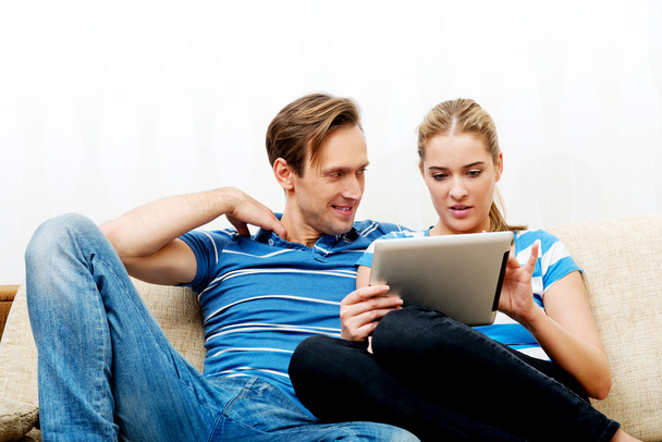 Νεαρό ζευγάρι κάθεται στο σπίτι και ψάχνει για κάτι στο tablet - Φωτογραφία, εικόνα