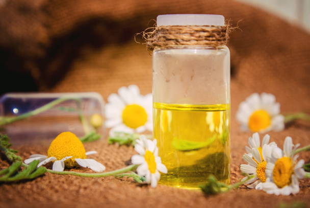 óleo fragrante de flores de camomila em uma garrafa de vidro macro na mesa de madeira horizontal
 - Foto, Imagem