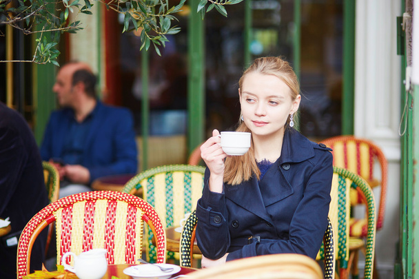 Beautiful young woman drinking hot chocolate in Parisian outdoor cafe  - Photo, Image