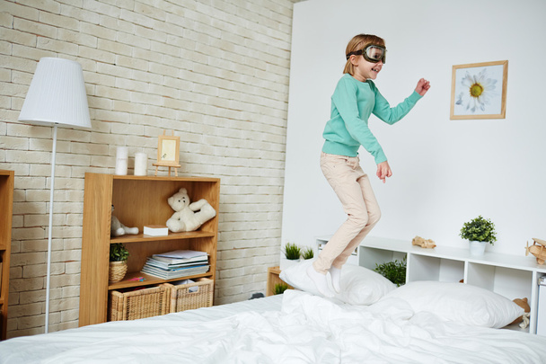 Chica en gafas piloto saltando en la cama
  - Foto, imagen