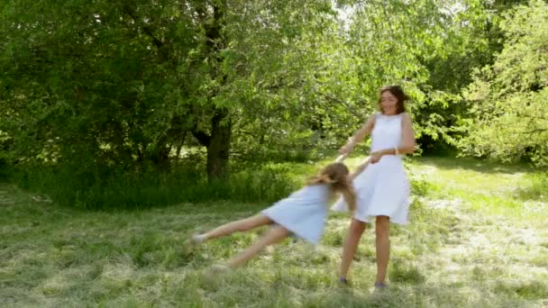 Mother and daughter playing in park, mom spinning her little girl - Materiał filmowy, wideo