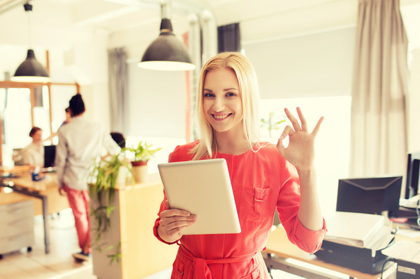 woman with tablet pc showing ok sign at office - Foto, afbeelding