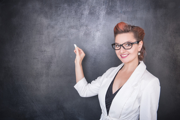Όμορφη δασκάλα με κομμάτι της κιμωλίας στον μαυροπίνακα φόντο - Φωτογραφία, εικόνα