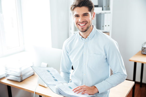 Cheerful young businessman holding folder with documents in office - 写真・画像
