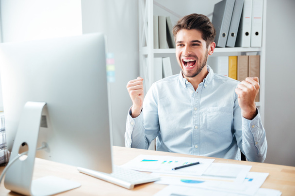 Happy excited young businessman sitting and celebrating success - Photo, Image