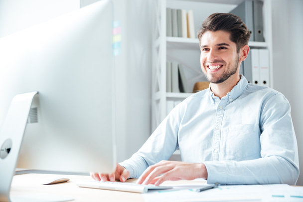 Sonriente joven hombre de negocios utilizando ordenador portátil en la oficina
 - Foto, Imagen