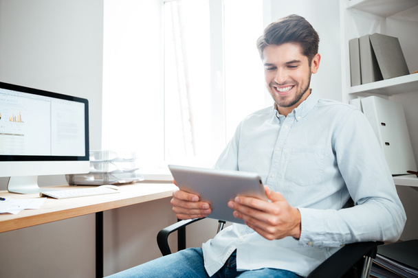 Smiling businessman sitting and using tablet computer in office - Valokuva, kuva