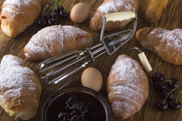 verse croissants met eieren, cherry jam en handvat mixer. - Foto, afbeelding
