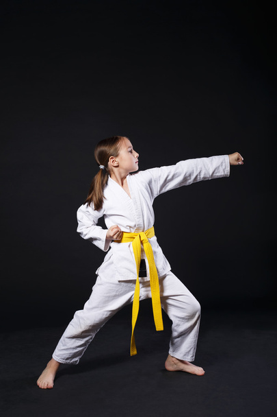 Дитяча дівчина в костюмі карате з жовтим поясом показує позицію
 - Фото, зображення