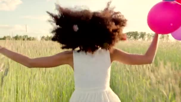 Menina correndo através de um campo de trigo com balões de cor durante o pôr do sol
 - Filmagem, Vídeo