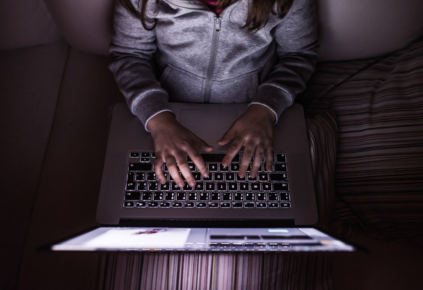 Unrecognizable girl, sitting in a dark, playing with laptop - Foto, imagen