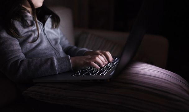 Laptop ile oynarken bir karanlıkta oturan tanınmayan kızı - Fotoğraf, Görsel