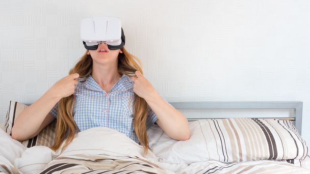 Kaunis nainen käyttää VR kuulokkeet sängyssä
 - Valokuva, kuva