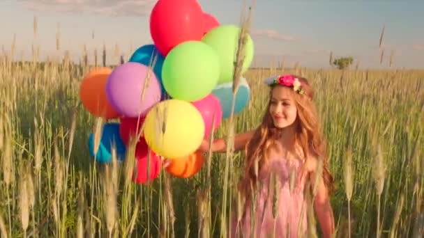 Young girl spinning around in wheat field with colour balloons during sunset - Materiał filmowy, wideo