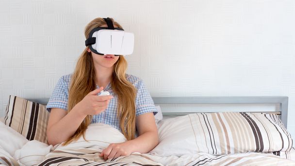 Beautiful woman using VR headset in bed - Foto, afbeelding