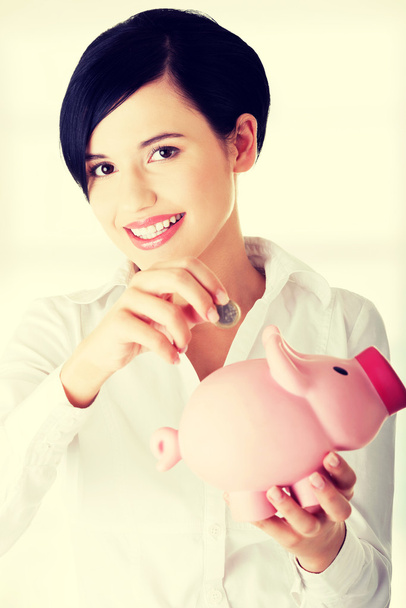Businesswoman putting a coin into a piggy bank - Фото, зображення