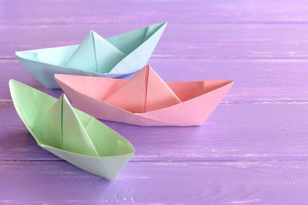 Bateaux en papier rose, vert, bleu sur fond lilas en bois. Techniques de pliage du papier. Artisanat origami facile pour les enfants à faire
 - Photo, image