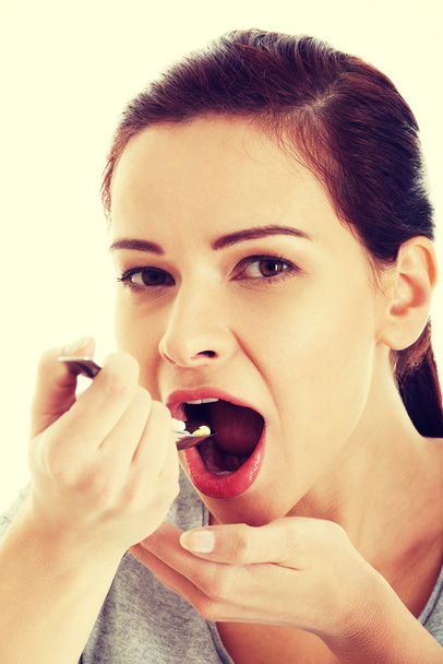Young casual woman eating pills on a spoon. - Foto, Imagem