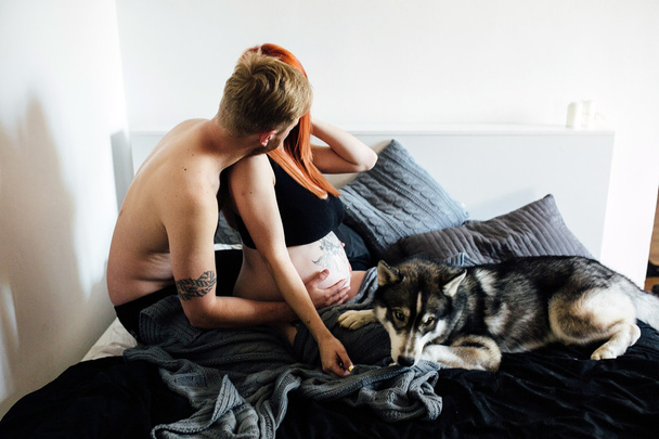 Mulher grávida, homem e cão sentados em uma cama
 - Foto, Imagem