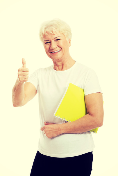 An old woman holding workbook and showing OK. - Фото, зображення