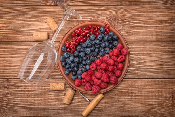 Wine glass with berries and corks on wooden table. - Фото, зображення
