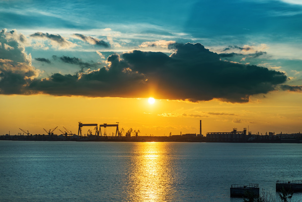 pôr do sol em nuvens escuras ao longo do rio e da construção naval da fábrica - Foto, Imagem
