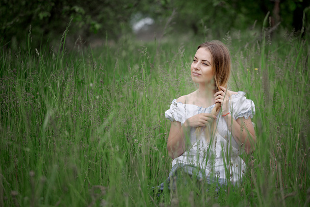 屋外の芝生の上に座っている短パンでブロンドの女の子 - 写真・画像