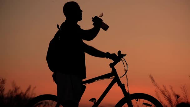 Cyclist drinks water from his canteen, silhouette at sunset - Video