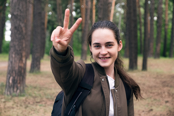 Happy teen girl backpacker showing peace sign at camera - Fotó, kép