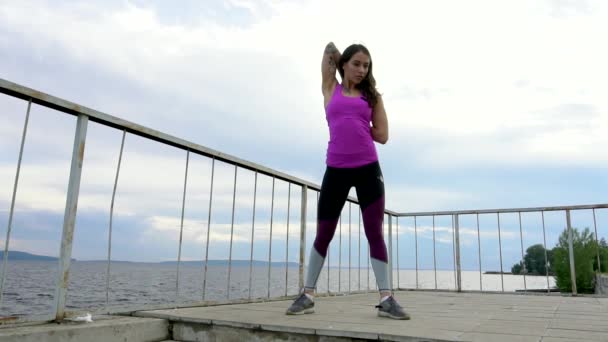 Fitness girl on the embankment of the river. Perform stretching. Slow motion. - Footage, Video