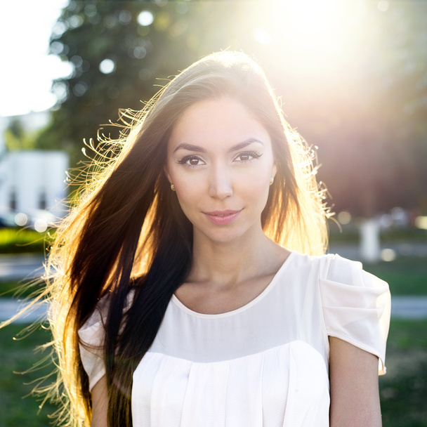 Portrait of a beautiful brunette in  park in bright sunlight. Fashion style  urban life, emotionally looks. Outdoor summer. - Foto, Imagen