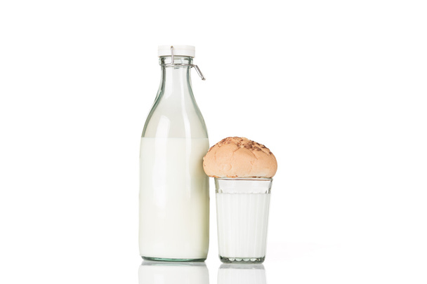 Faceted glass of milk with a bun on it stands near closed old fashioned bottle of milk. - Photo, Image