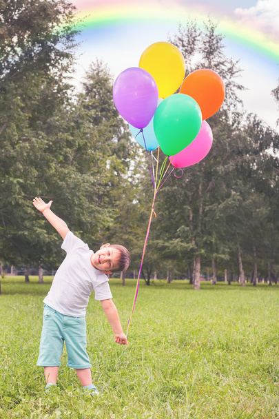 Gelukkig kind met ballonnen en mooie regenboog buiten - Foto, afbeelding