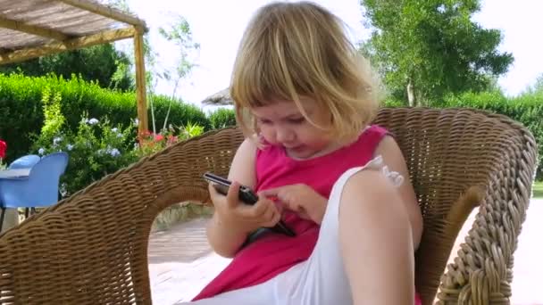 baby sitting in wicker chair calling with mobile phone - Footage, Video