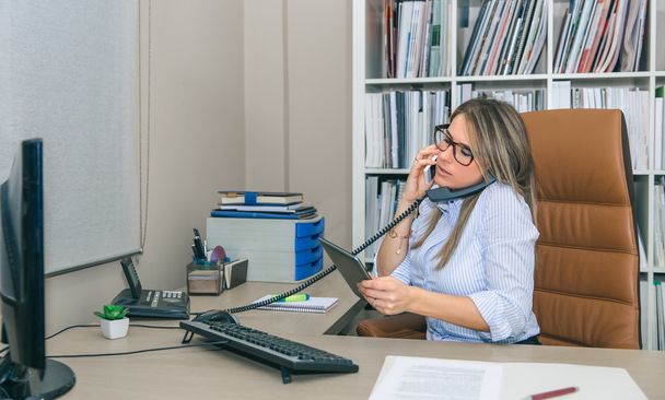 Занятая деловая женщина разговаривает с сотовым и стационарным телефоном в офисе
 - Фото, изображение