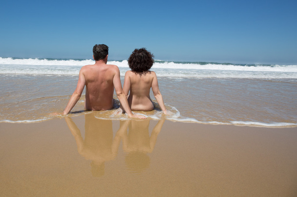 Casal na água na praia, de costas para a câmera
 - Foto, Imagem
