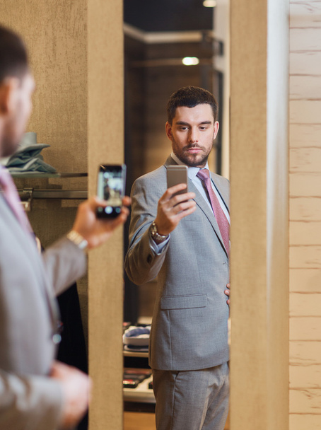 man in suit taking mirror selfie at clothing store - Фото, изображение