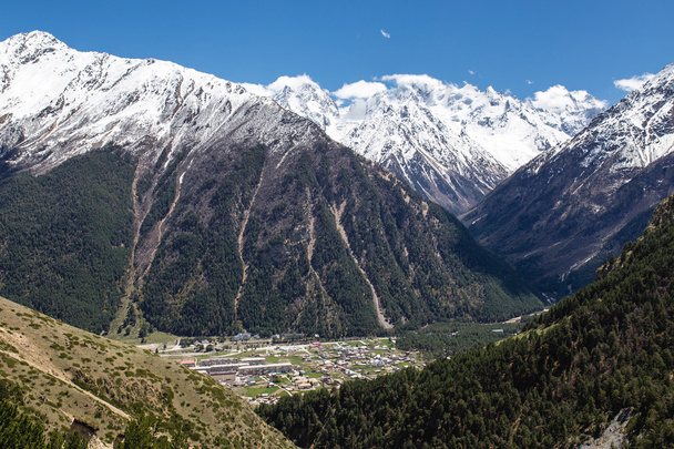 górska ścieżka i wieś w dolinie na tle ośnieżonych szczytów - Zdjęcie, obraz