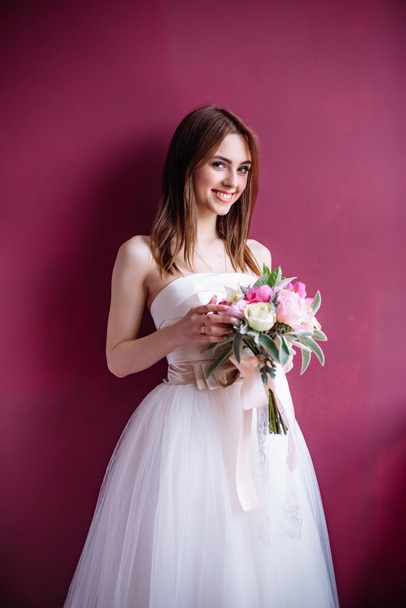 young beautiful bride with a bouquet of pink peony near the wall - Fotografie, Obrázek