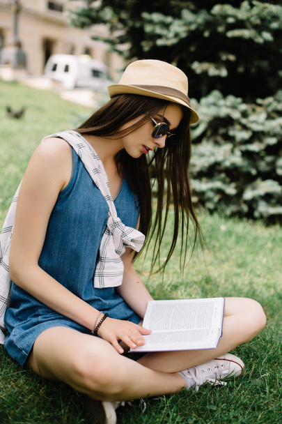 Młoda kobieta siedząca na trawie i czytająca książkę.  - Zdjęcie, obraz