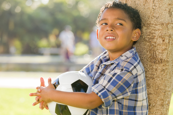 chłopiec mieszanej rasy posiadania piłki nożnej w parku z drzewa - Zdjęcie, obraz