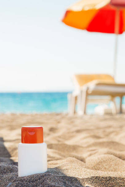 Бутылка крема от солнца в тени на пляже
 - Фото, изображение