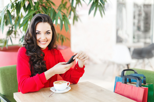 Όμορφο κορίτσι στο καφέ στο εμπορικό κέντρο με καφέ και τηλέφωνο - Φωτογραφία, εικόνα