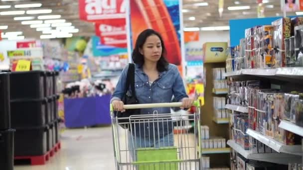 Asian girl, woman walking, looking and pushing shopping cart in supermarket isle - Filmagem, Vídeo